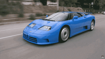 A Blue Sports Car Is Driving Down A Street With A Sign That Says No Parking GIF