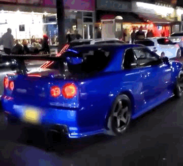 A Blue Sports Car Is Parked On The Street In Front Of A Store Called Rio GIF