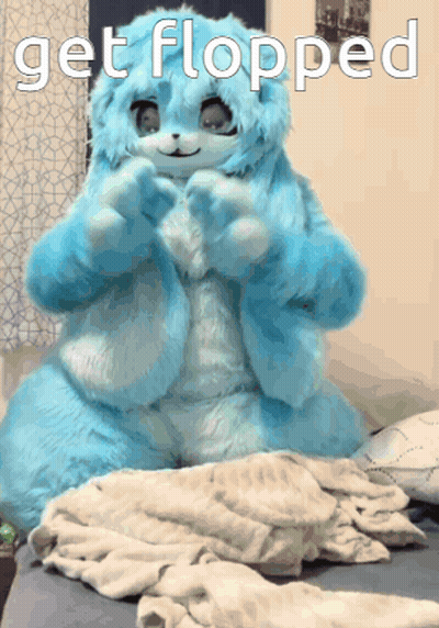 A Blue Stuffed Animal Is Sitting On A Bed With The Words Get Flopped Below It GIF