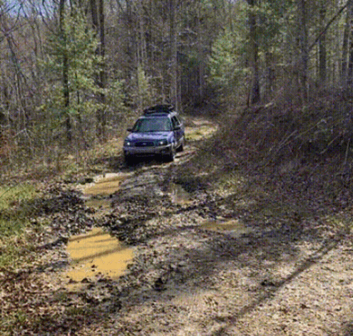 A Blue Suv With A Roof Rack Is Driving Down A Muddy Road GIF