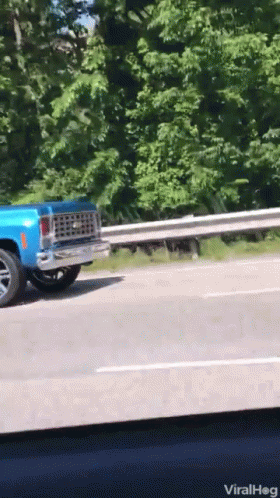 A Blue Truck Is Driving Down A Highway With A Railing Behind It GIF