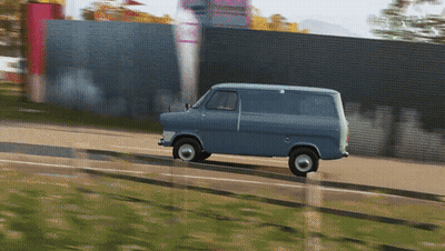 A Blue Van Is Driving Down A Road In Front Of A Fence GIF