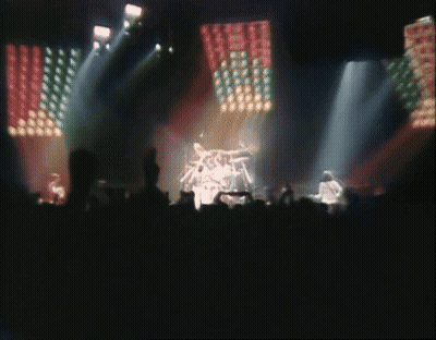 A Blurred Image Of A Band On Stage With A Crowd Watching GIF