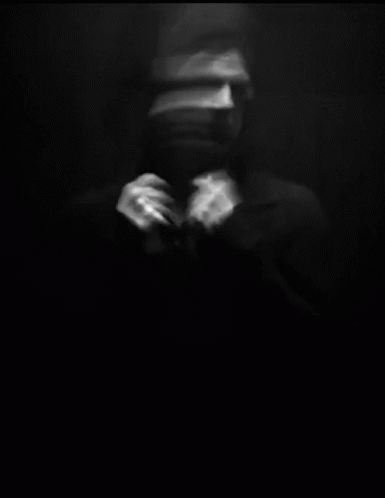 A Blurry Black And White Photo Of A Man Adjusting His Tie In A Dark Room . GIF