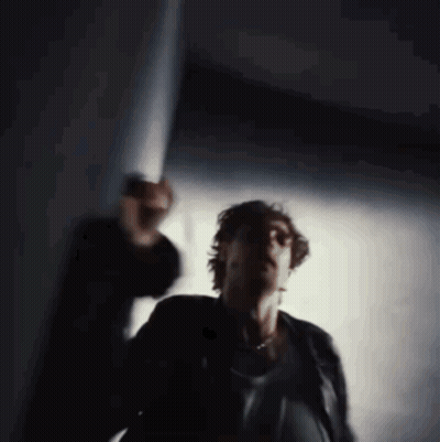 A Blurry Photo Of A Man In A Black Jacket Standing In A Dark Room GIF