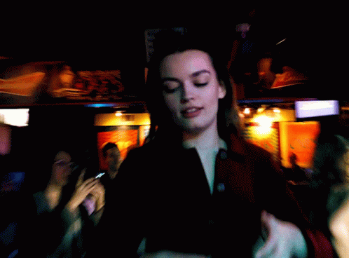 A Blurry Photo Of A Woman In A Dark Room With A Sign That Says ' Coca Cola ' On It GIF