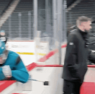 A Blurry Picture Of A Hockey Game With A Man Wearing A Black Jacket That Says Reebok On It GIF