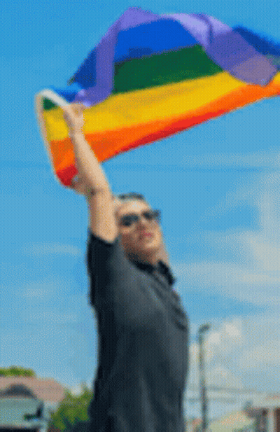 A Blurry Picture Of A Man Holding A Rainbow Flag In The Air . GIF