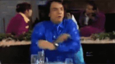 A Blurry Picture Of A Man In A Blue Shirt And Tie Sitting At A Table GIF