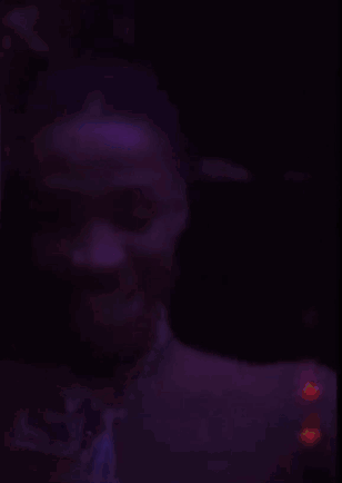 A Blurry Picture Of A Man In A Dark Room With Purple Lights Behind Him GIF