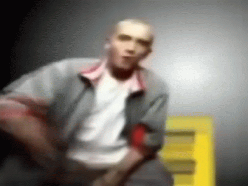 A Blurry Picture Of A Man In A Gray Jacket And White Shirt Standing In Front Of A Yellow Sign . GIF