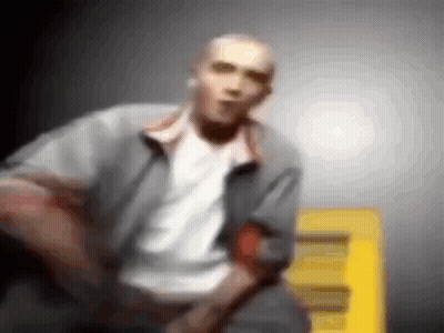 A Blurry Picture Of A Man In A Gray Jacket And White Shirt Standing Next To A Yellow Sign . GIF