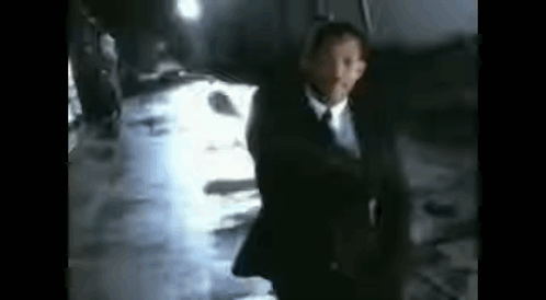 A Blurry Picture Of A Man In A Suit And Tie Walking Down A Hallway . GIF