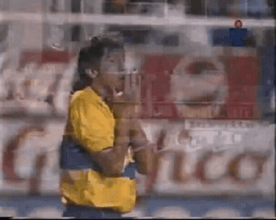 A Blurry Picture Of A Man In A Yellow Shirt Standing In Front Of A Sign That Says ' Coca Cola ' GIF