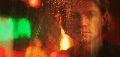 A Blurry Picture Of A Man 'S Face Behind A Window With A Green Light Behind Him GIF