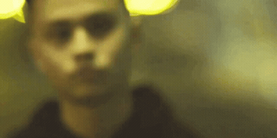 A Blurry Picture Of A Man 'S Face In A Dark Room With A Yellow Light Behind Him . GIF