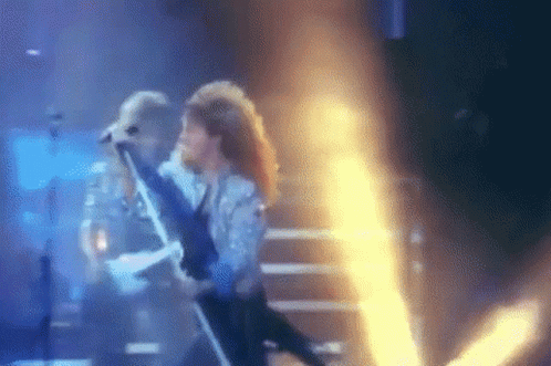 A Blurry Picture Of A Man Singing Into A Microphone On A Stage GIF