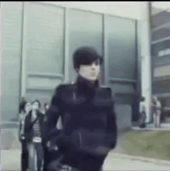A Blurry Picture Of A Man Wearing Sunglasses And A Hat Walking In Front Of A Building . GIF