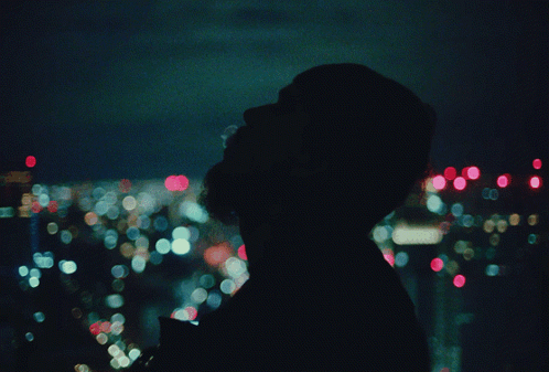 A Blurry Picture Of A Person Looking Out A Window At A City At Night GIF
