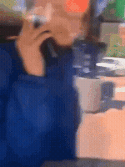 A Blurry Picture Of A Person Sitting At A Table Talking On A Cell Phone GIF