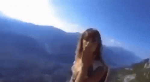 A Blurry Picture Of A Woman Covering Her Face In Front Of A Mountain Range . GIF