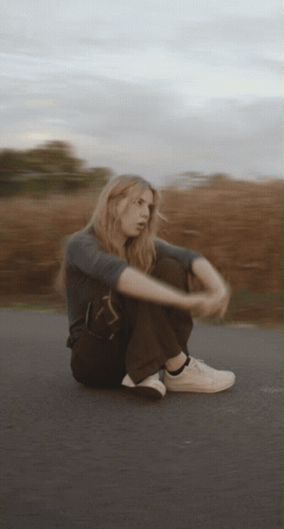 A Blurry Picture Of A Woman Sitting On The Side Of A Road GIF