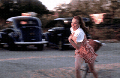 A Blurry Picture Of A Woman Walking Down A Street With A Car In The Background GIF