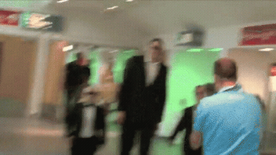 A Blurry Picture Of People Walking In A Hallway With A Red Sign That Says Exit GIF