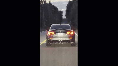 A Bmw Is Driving Down A Road With Trees On Both Sides GIF