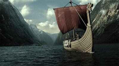 A Boat With A Red Sail Is In The Middle Of A River GIF