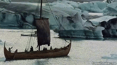 A Boat With A Sail Is In The Water With Icebergs In The Background GIF