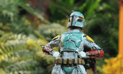 A Boba Fett Action Figure Is Standing In The Woods With His Arms Crossed . GIF