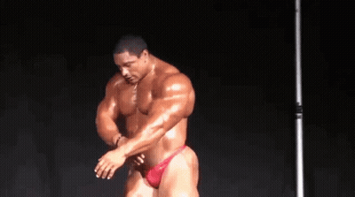 A Bodybuilder In A Red Underwear Is Standing In Front Of A Black Background And Flexing His Muscles . GIF