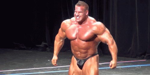 A Bodybuilder Is Standing On A Stage With His Arms In The Air GIF