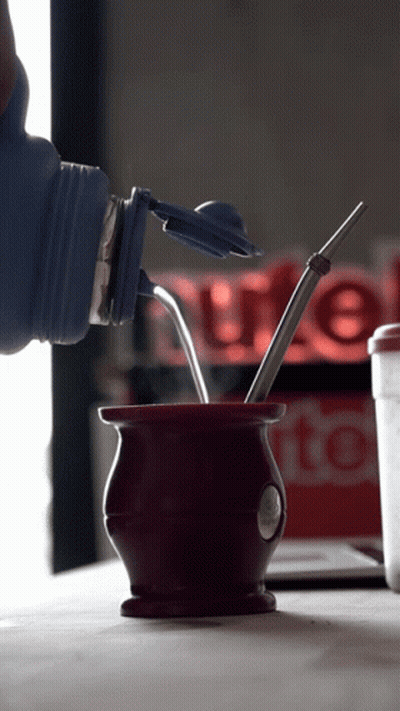 A Bottle Is Being Poured Into A Cup With A Straw In It GIF