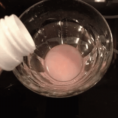 A Bottle Is Being Poured Into A Glass Of Liquid GIF