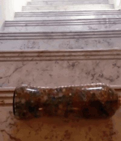 A Bottle Is Sitting On A Marble Floor In Front Of Stairs GIF