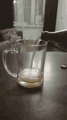 A Bottle Of Beer Is Being Poured Into A Glass Mug On A Table GIF