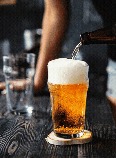 A Bottle Of Beer Is Poured Into A Glass On A Wooden Table GIF