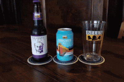 A Bottle Of Bell 'S Beer Sits Next To A Glass And A Can GIF
