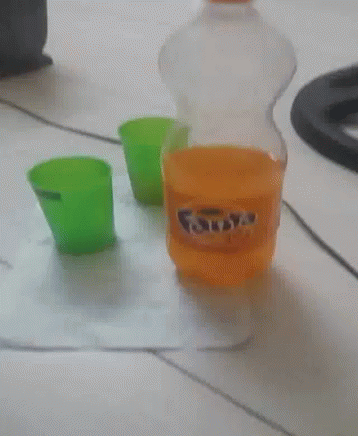 A Bottle Of Fanta Sits On A Table Next To A Green Cup GIF