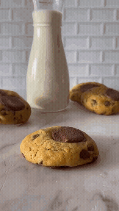 A Bottle Of Milk Sits Next To Three Cookies GIF