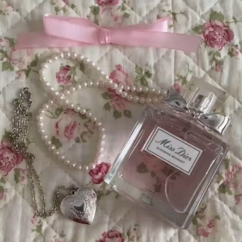 A Bottle Of Miss Dior Perfume Sits On A Floral Quilt GIF