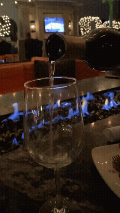 A Bottle Of Wine Is Being Poured Into A Glass On A Table GIF