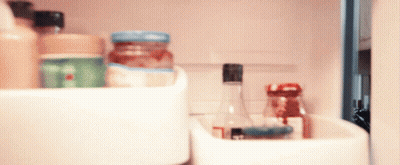 A Bottle With A Black Cap Sits In A Refrigerator Shelf GIF