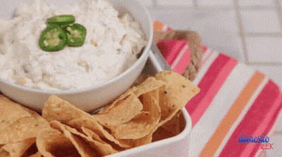A Bowl Of Dip With Jalapenos On Top Next To A Bowl Of Chips GIF