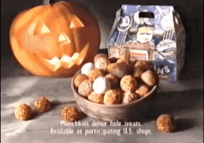 A Bowl Of Donut Hole Treats Next To A Pumpkin With A Face Carved Into It GIF