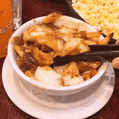A Bowl Of Food With Tongs On A Plate With A Bottle Of Orange Juice In The Background GIF