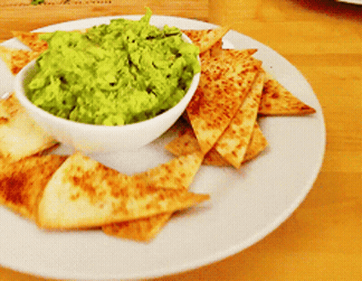 A Bowl Of Guacamole Sits On A Plate With Tortilla Chips GIF