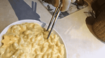 A Bowl Of Macaroni And Cheese Is Being Served With Chopsticks GIF